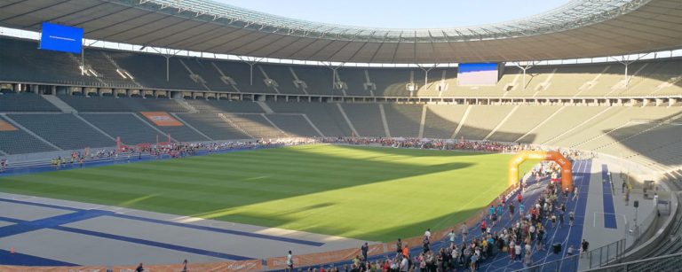 Firmenlauf B2Run in einem Stadion mit leeren Rängen und einer blauen Laufbahn voller Menschen