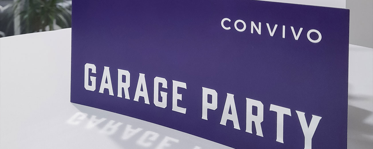 Blauer Flyer mit dem convivo Logo und der Headline "Garage Party" in Versalien auf einem weißen Tisch, im unscharfen Hintergrund sind Pflanzen zu sehen