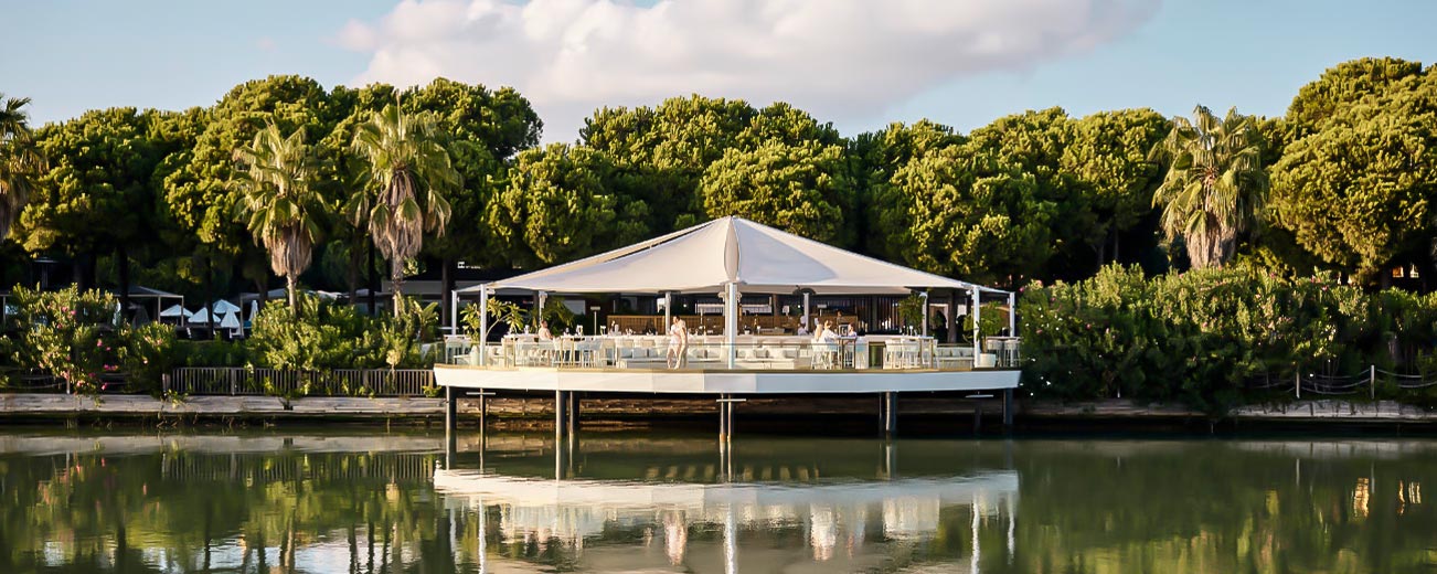 Bar auf einem Steg vor einem Wald auf dem Gelände des Club Robinson Resorts, unten im Vordergrund ist das Meer oder ein Kanal zu sehen, im hintergrund blauer Himmel mit einer Wolke